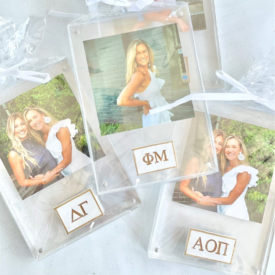 A Sorority Acrylic Frame with two clear acrylic panels and a white and gold medallion featuring greek letters. The frame contains a photo of two individuals.